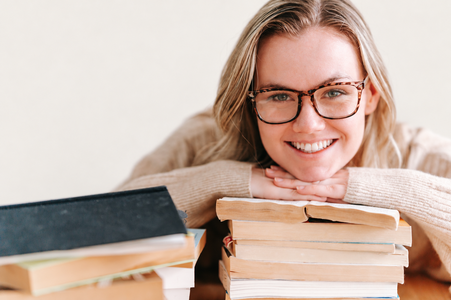 Una giovane sorridente con gli occhiali appoggiata a una pila di libri